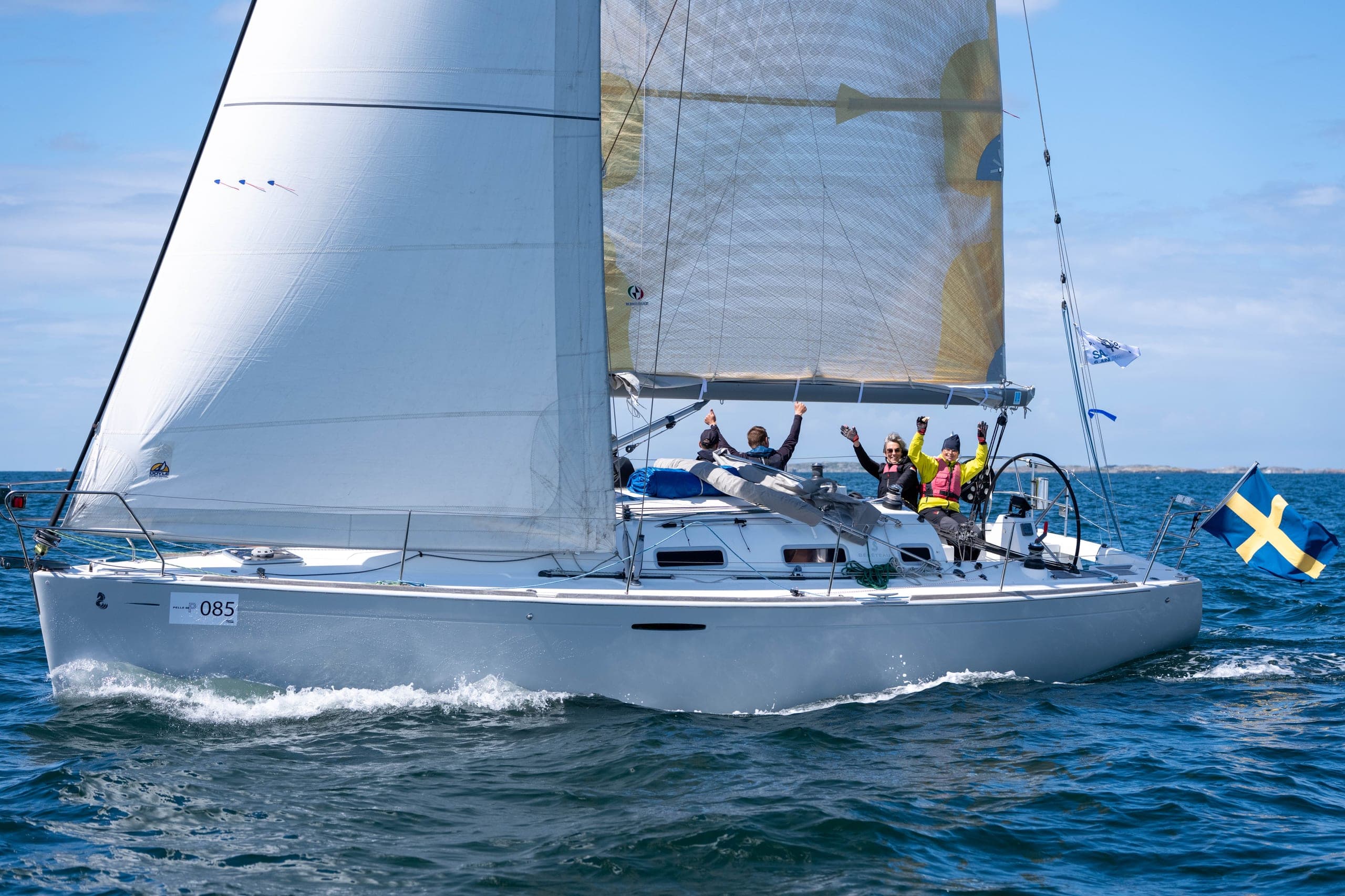 Besättning som jublar med armarna i luften under gyllene spinnaker