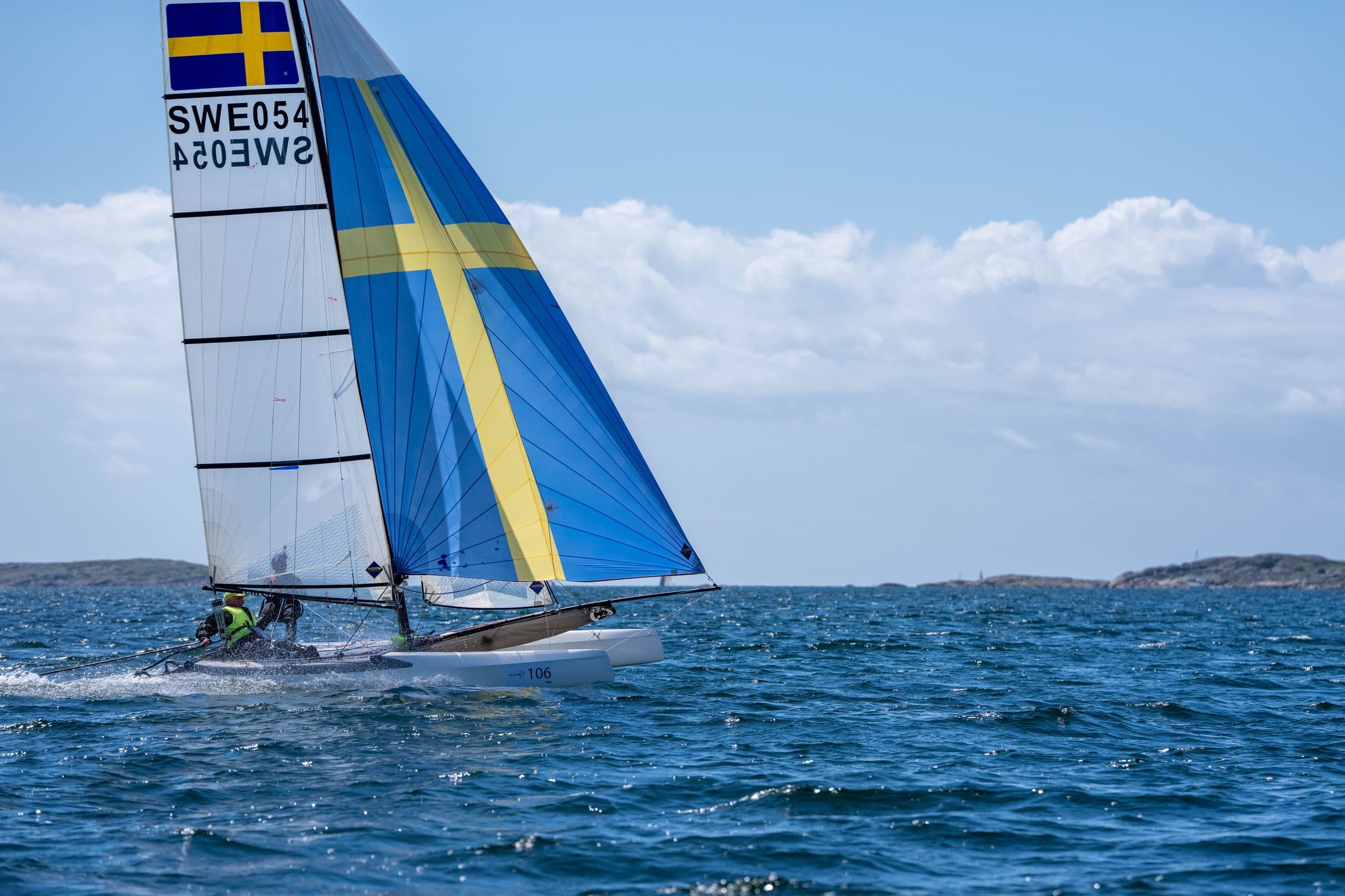 Katamaran med blågul spinnaker i öppet vatten